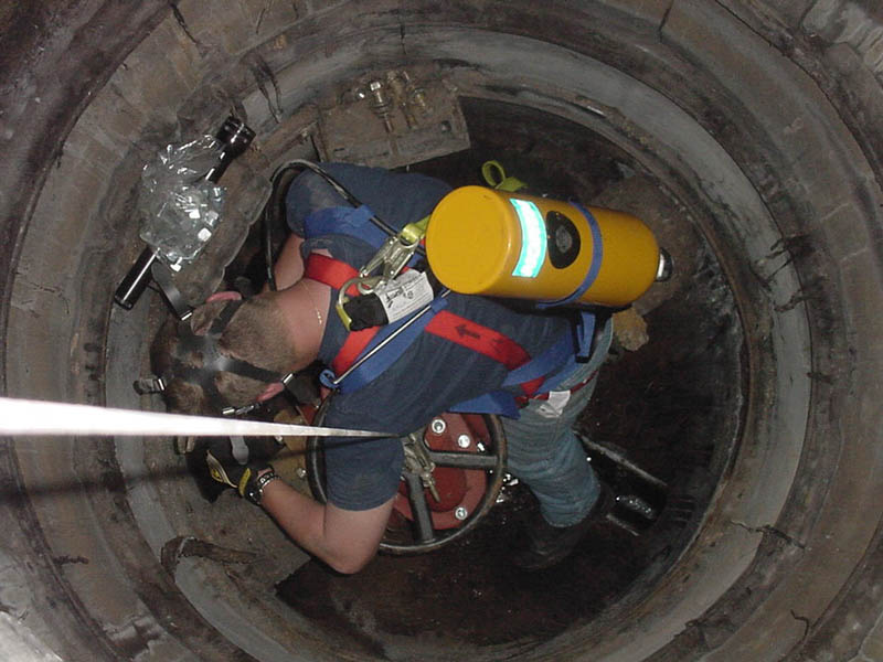 A man in blue shirt and yellow vest working inside of pipe.