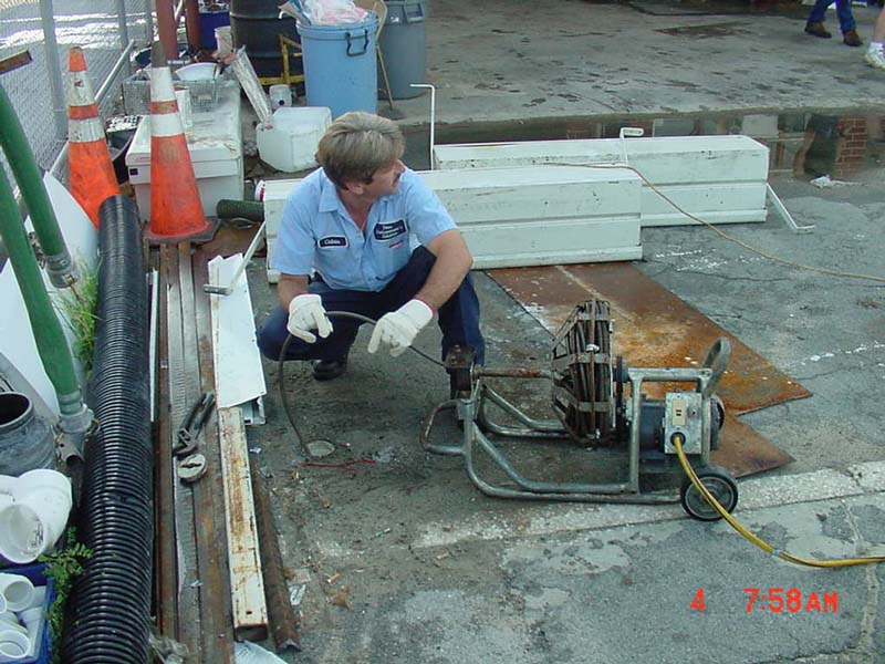 A man in white gloves kneels down next to a pipe.