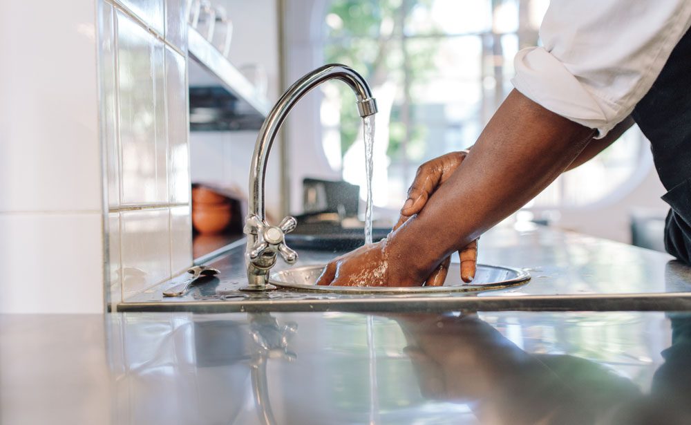 A person washing their hands in the kitchen sink.